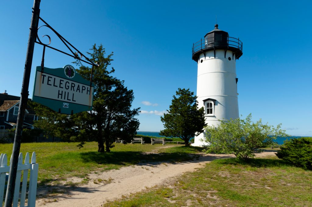 A sign reading Telegraph Hill in front of a dirt path leading to a white lighthouse.