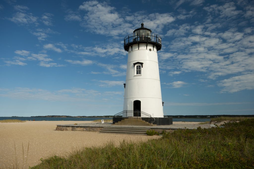 A tall white lighthouse with black trim on a peaceful beach.