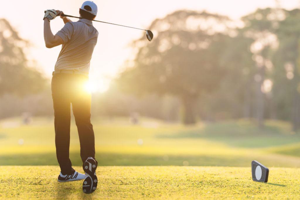 A man swinging a golf club into the sun on a sunny morning at a golf course in Plymouth, MA